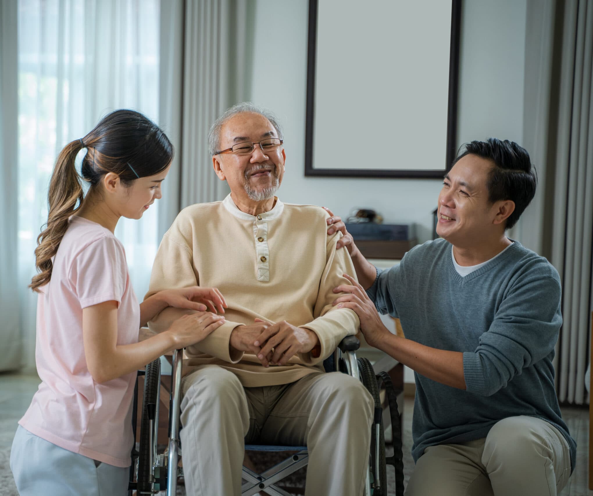 An older man in a wheelchair with two family members beside him