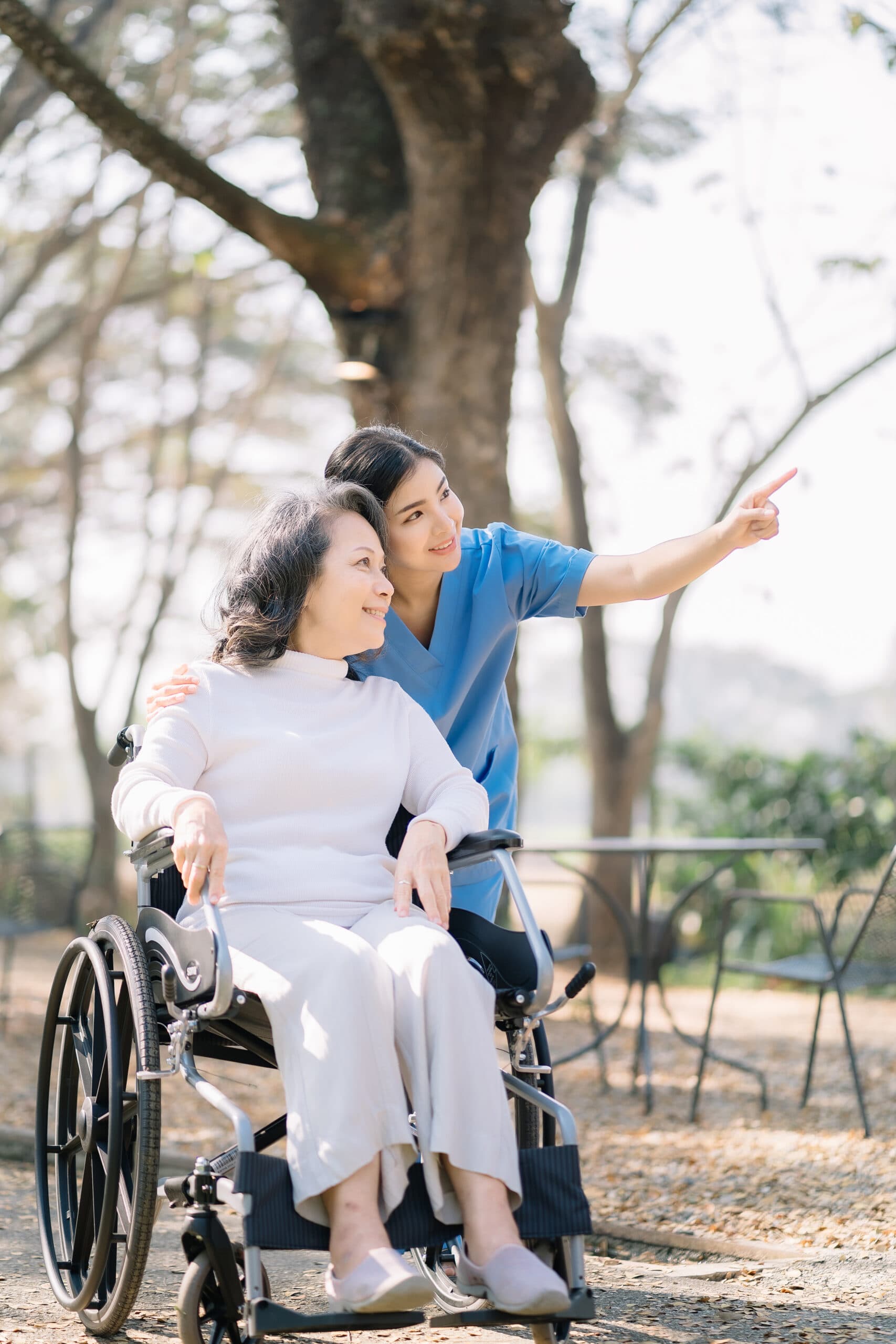 A carer walking with an older woman in a wheelchair outdoors