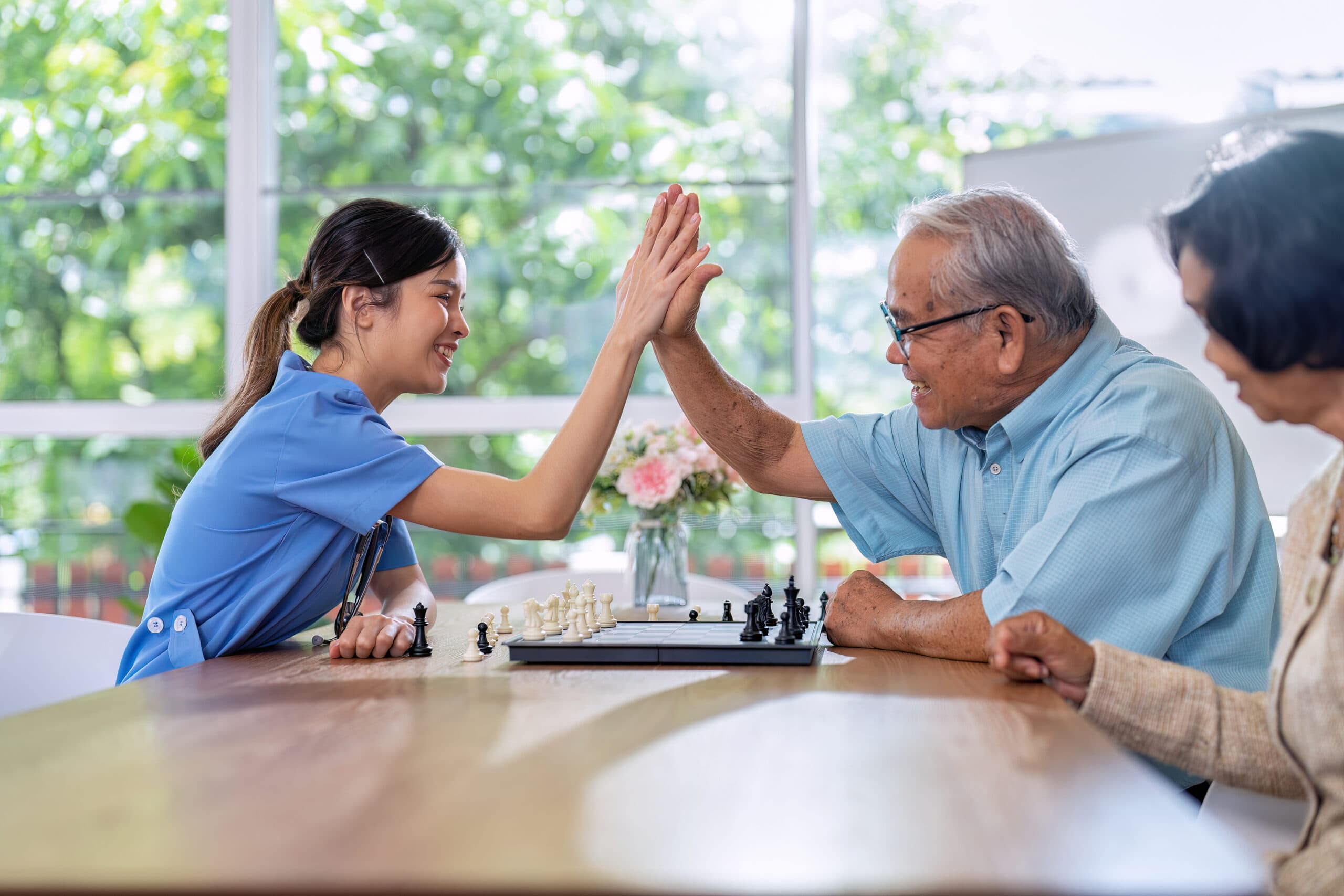 A carer and an older man high-fiving over a game of chess