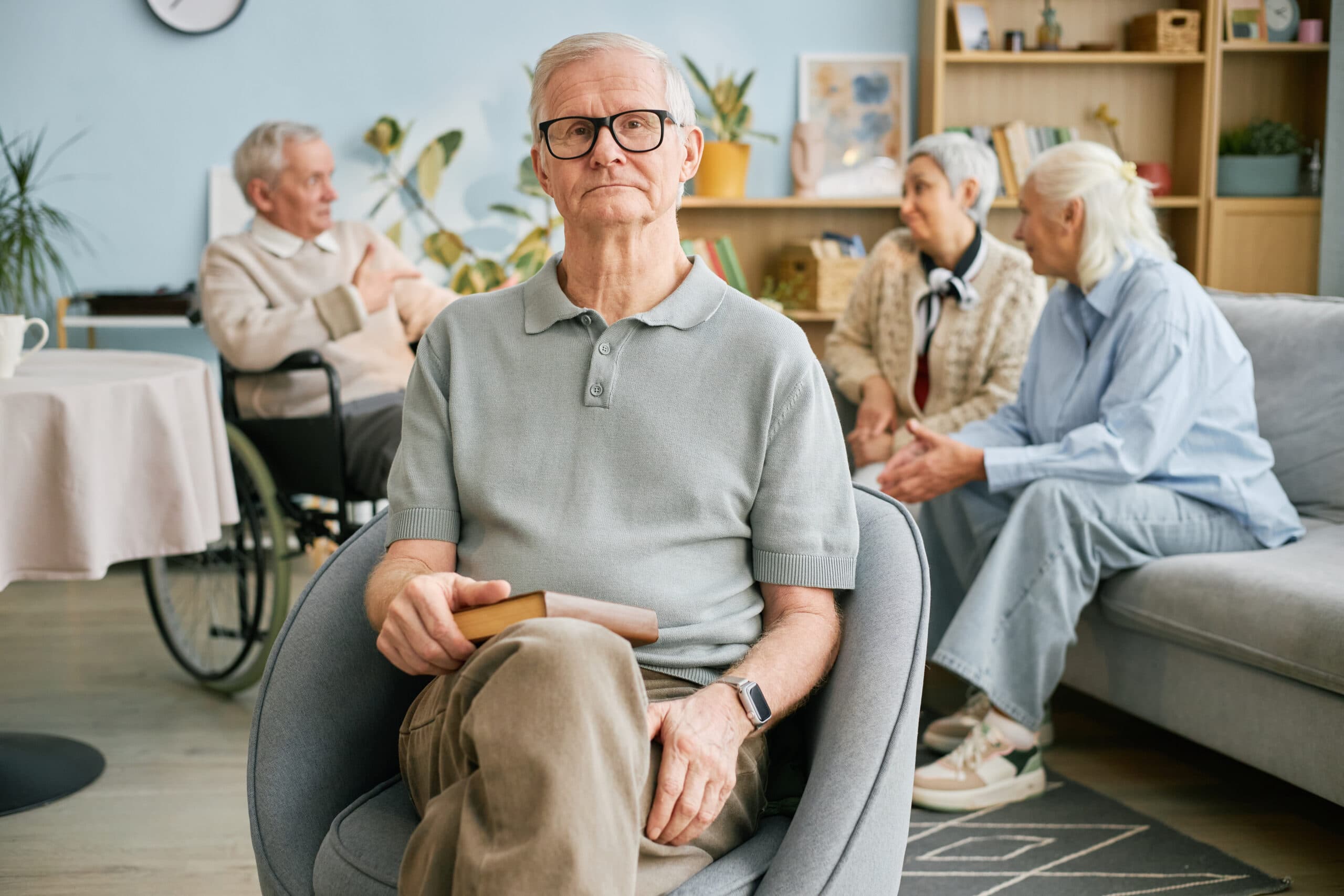 An older man seated in an aged care home lounge with other residents